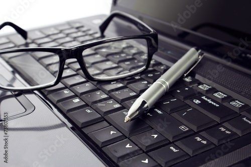 Businessman's glasses and pen on laptop computer
