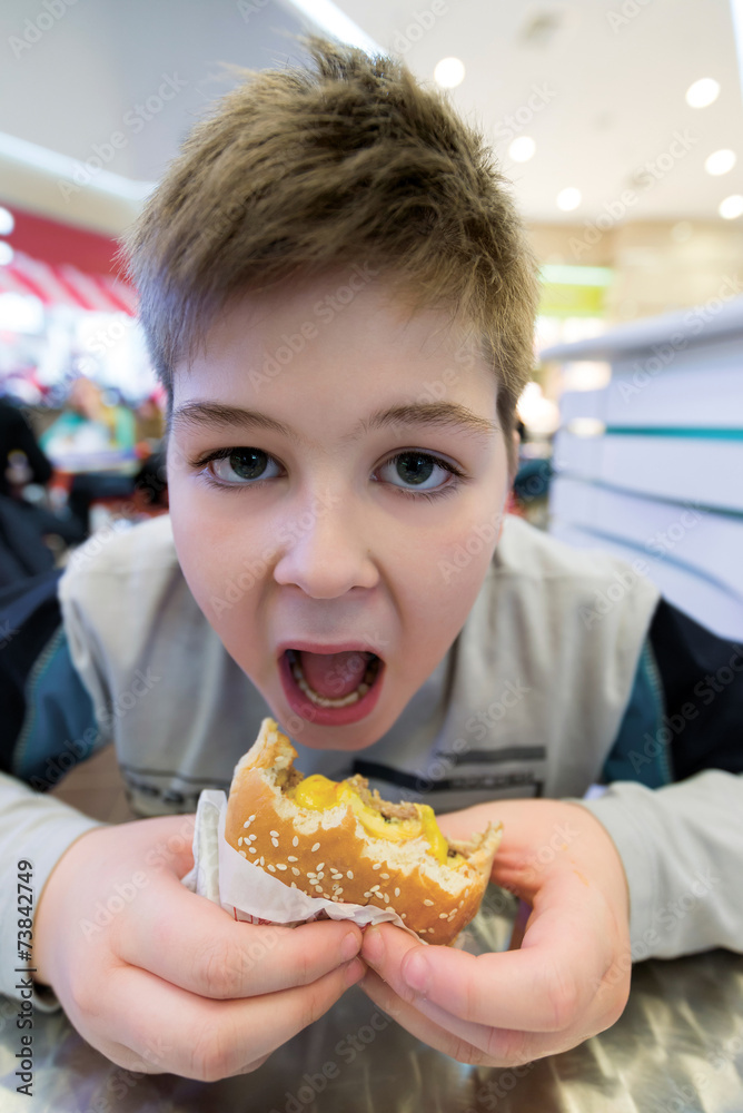 Teen boy eats  hamburger n Cafe