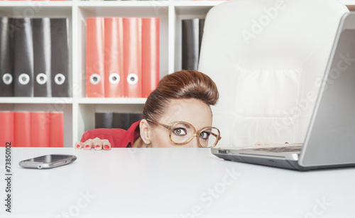 Quadro em tela Business woman hiding behind table and afraid