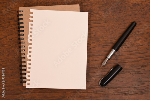 Pen and notebook on wooden background.