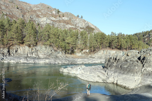 The man with a backpack standing at the mountain river