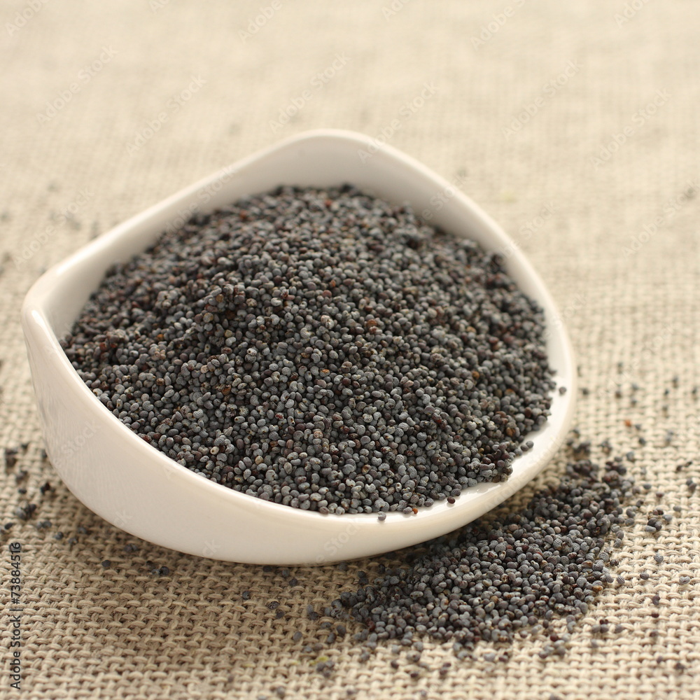 Poppy seeds in white ceramic bowl on sackcloth background Poppy seeds in white ceramic bowl on sackcloth background