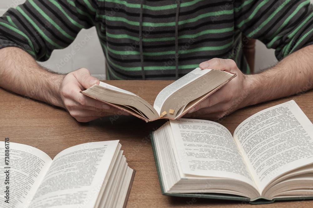 Man reading a book and other books open on the table Man reading a book and other books open on the table
