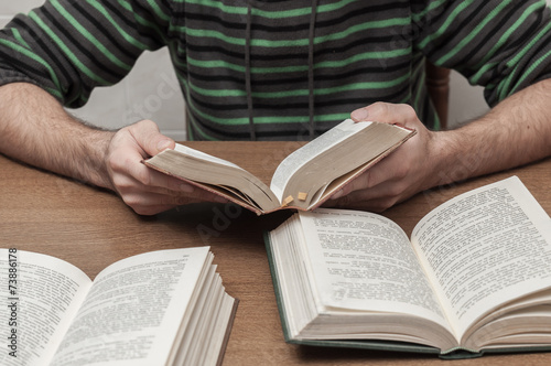 Man reading a book and other books open on the table