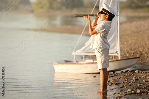 Boy captain looking through a telescope at the lake