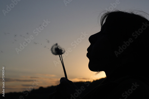 Woman in nature, blowing air to dandelion