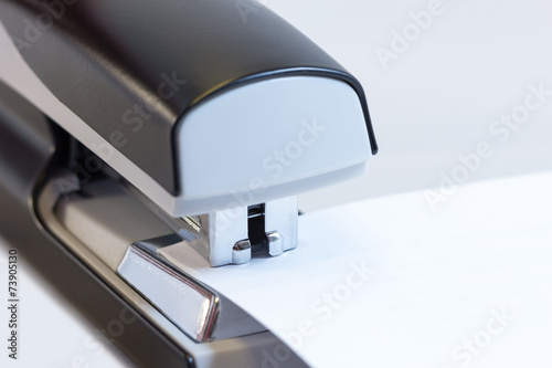 Closeup of a grey office stapler stapling white paper photo