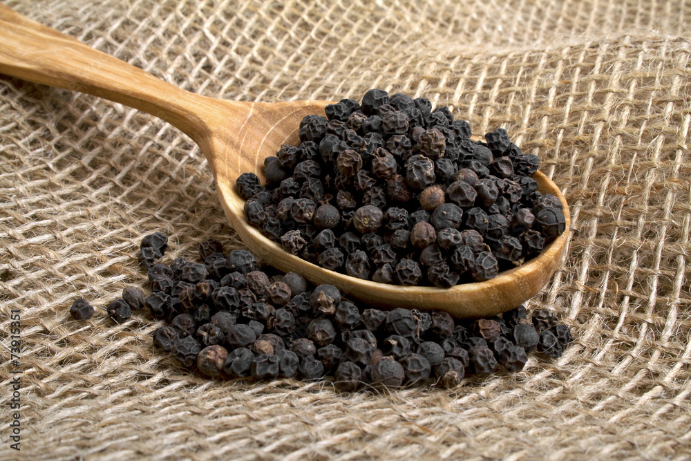 Black pepper in wooden spoon on burlap background Black pepper in wooden spoon on burlap background