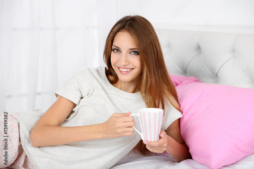 Young beautiful woman lying in bed with cup of hot drink