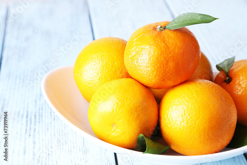 Tangerines with leaves on plate on wooden background