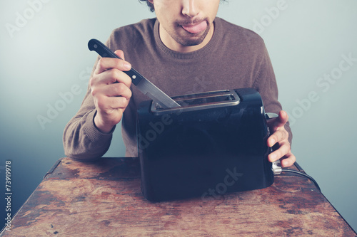 Vászonkép Young man sticking knife in toaster