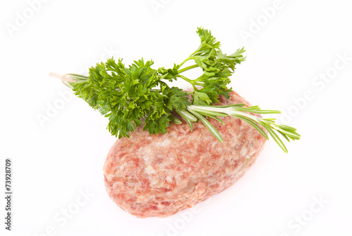 raw meat cutlet with a sprig of parsley and rosemary on a white