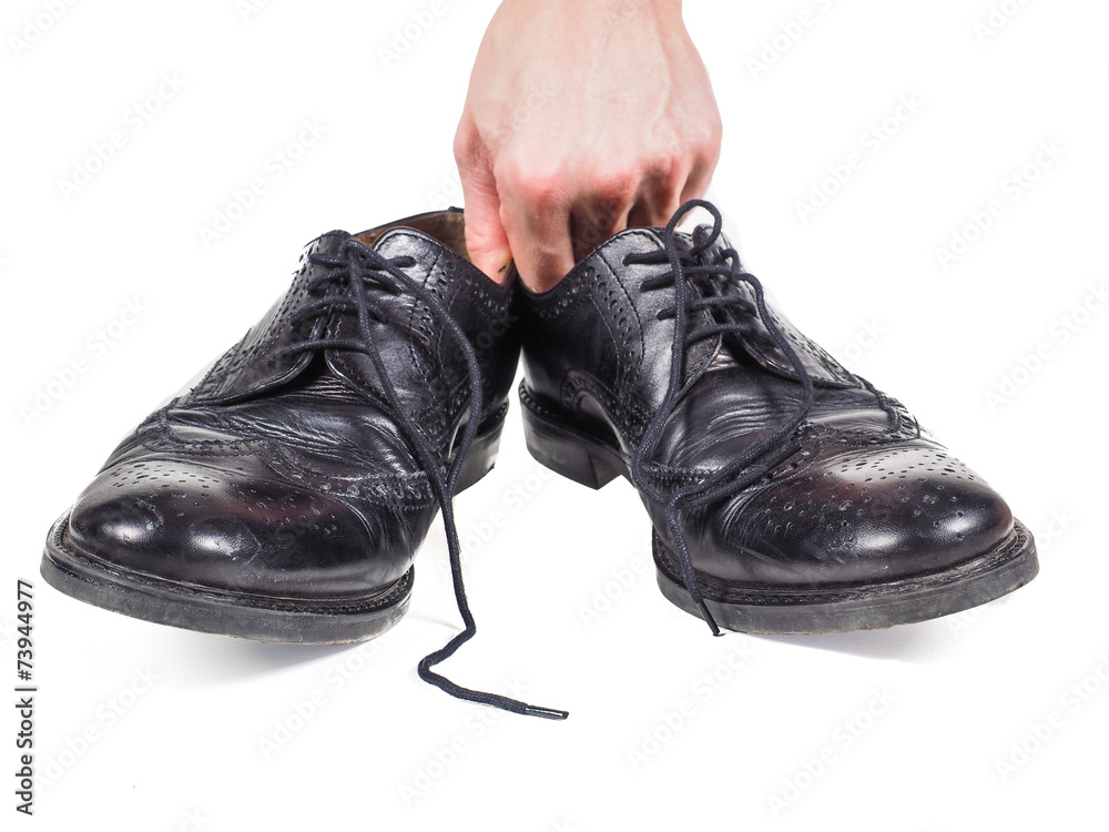 Male hands holding up a pair of worn black leather shoes towards