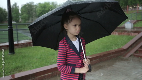 Lonely child girl in the rain under an umbrella slow motion. photo