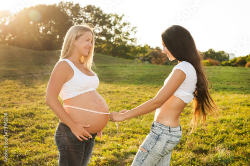Young woman measuring her pregnant friend's belly.
