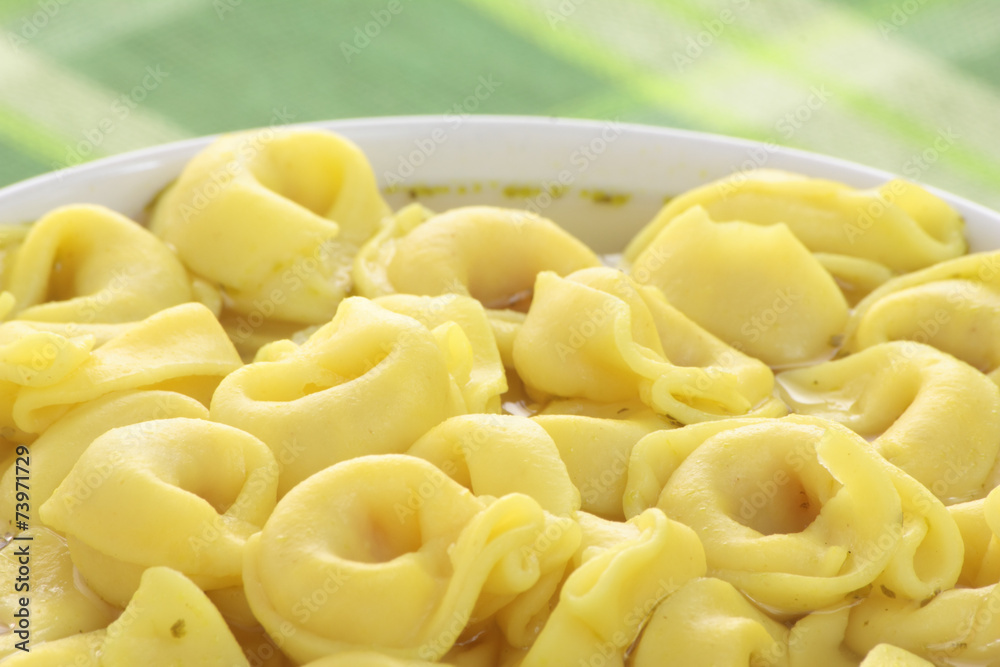 Bowl of chicken broth and tortellini on a green tablecloth.