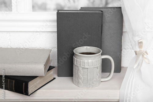Old books and cup of coffee on windowsill