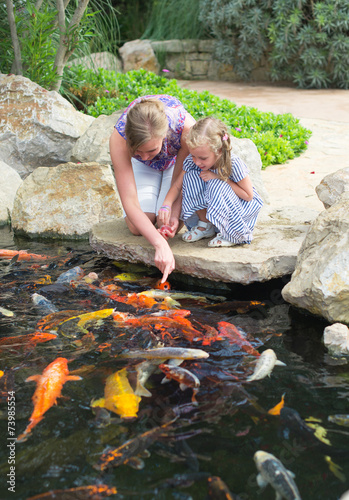 Bild auf Leinwand Woman and daughter feeding fishes in pond.