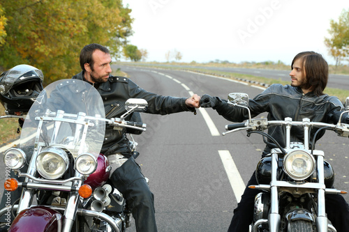 Two bikers on motorcycles handshaking with knuckle on road photo