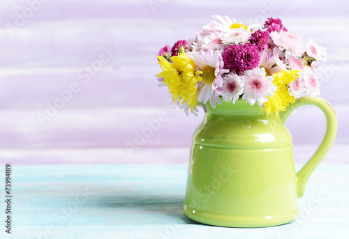 Fototapeta Naklejka Na Ścianę i Meble -  Beautiful flowers in pitcher on table on purple background