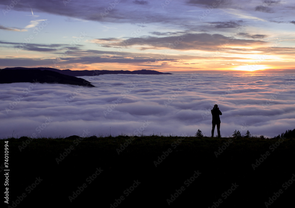 silhouetted photographer standing above fog on hill