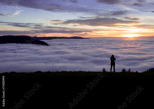 silhouetted photographer standing above fog on hill