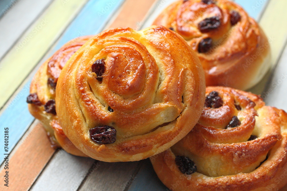Fototapeta premium Fresh sweet swirl buns with raisins on colored wooden table