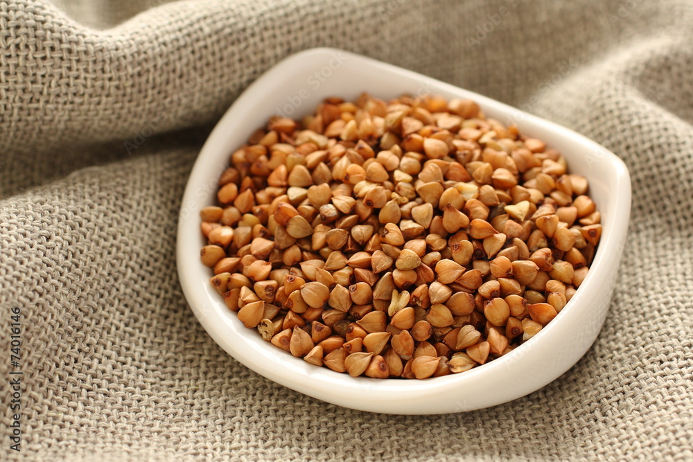 Buckwheat grains in white ceramic bowl on sackcloth background Buckwheat grains in white ceramic bowl on sackcloth background