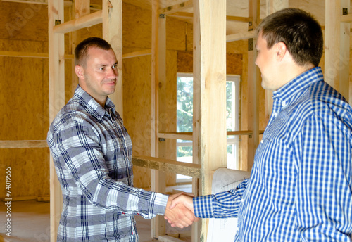 Two men shaking hands in a new build house