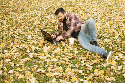 Man Laying Down In Autumn Leaves Using Laptop Computer