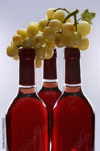 Three bottles of wine and holding a bunch of grapes
