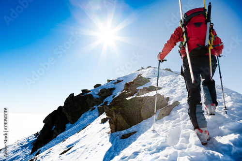 Climber walking up along a steep snowy ridge with the skis in t