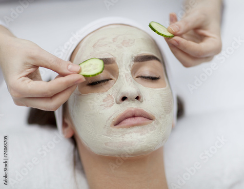Beautiful young woman receiving facial mask of cucumber in beaut