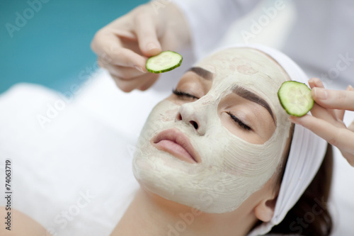 Beautiful young woman receiving facial mask of cucumber in beaut