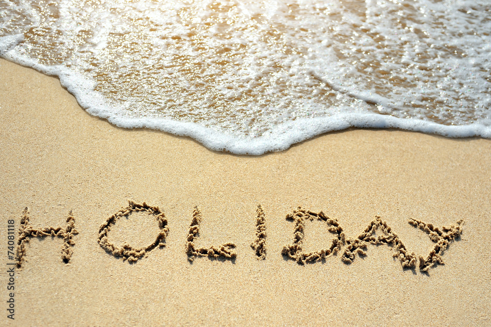 Fototapeta premium holiday written on the sand beach near sea