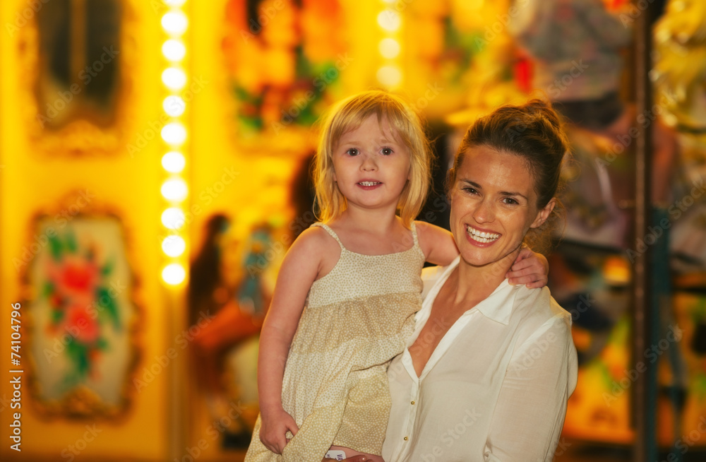 Portrait of happy mother and baby girl in front of carousel