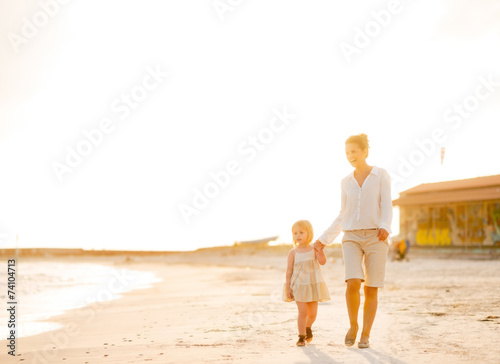 Happy mother and baby girl walking on beach at the evening © Alliance