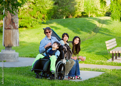 Disabled boy in wheelchair with family outdoors on sunny day sit