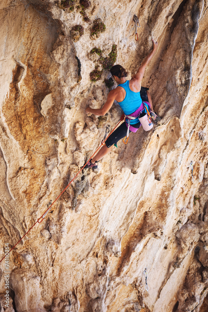 Young female rock climber on a face of a cliff