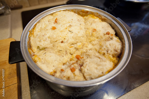 Thick dumplings in a turkey stew cooking on a stove top.