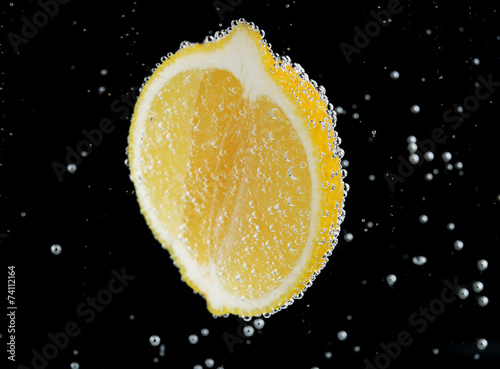 Fresh lemon in water with bubbles on black background