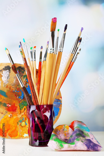 Paint brushes with paints and palette on bright background