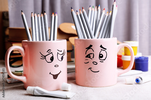 Emotional cups with pencils and paints on table