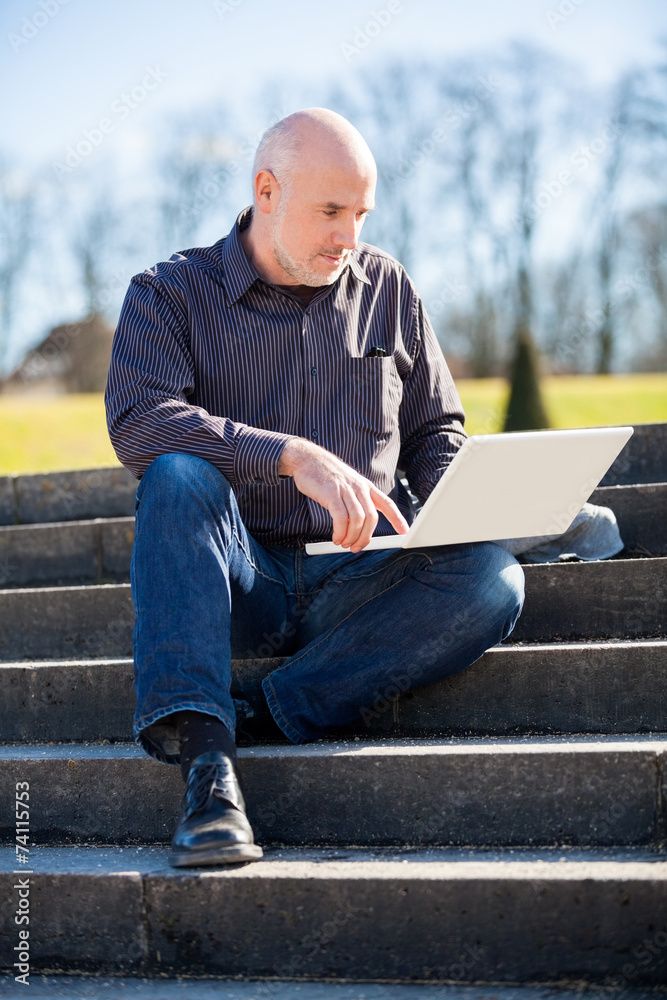 Obraz premium Man sitting on a bench using a laptop