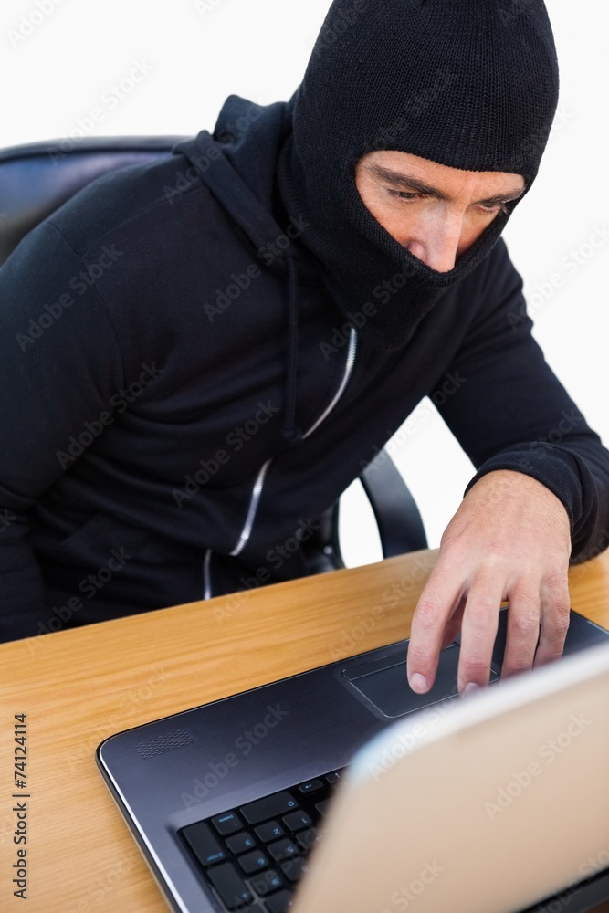 Thief with balaclava hacking a laptop Thief with balaclava hacking a laptop