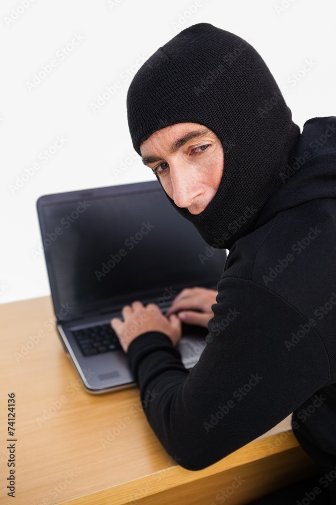 Burglar hacking a laptop and looking behind him Burglar hacking a laptop and looking behind him