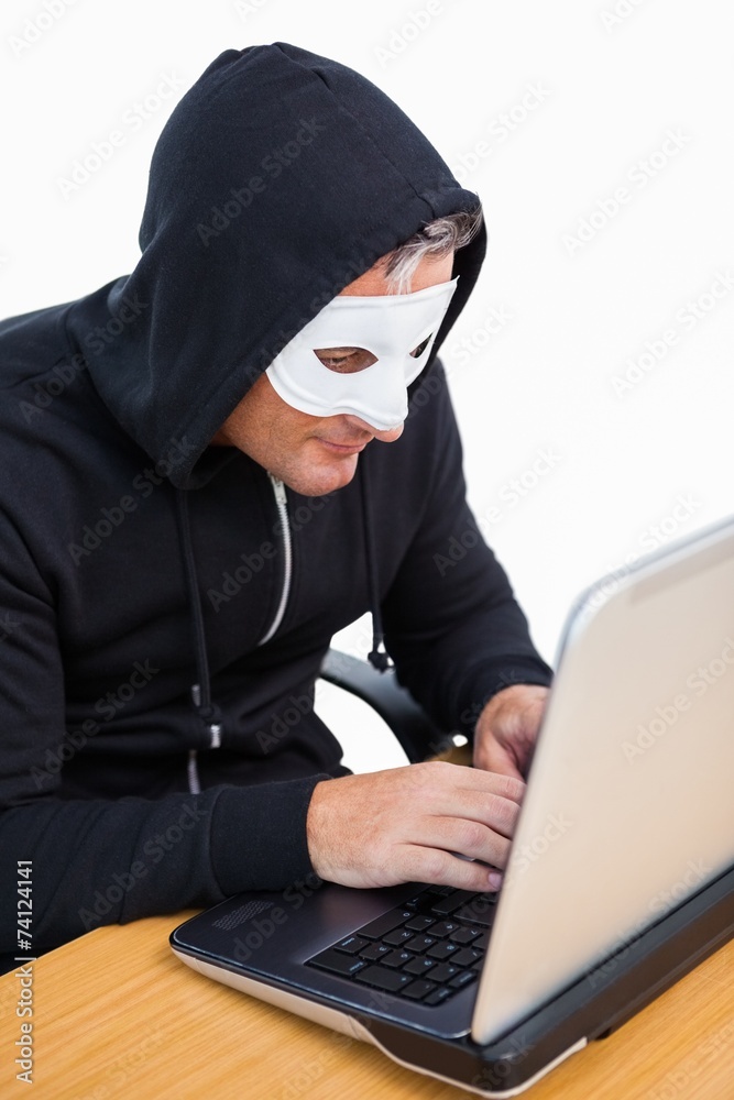 Burglar with white mask hacking a laptop Burglar with white mask hacking a laptop