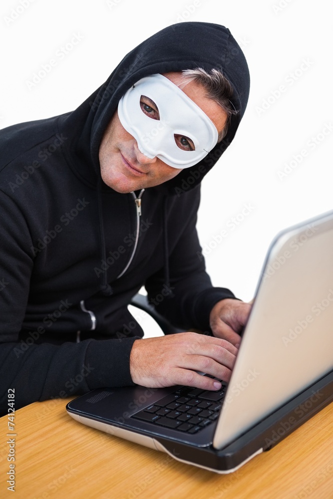 Hacker with white mask using laptop and looking at camera Hacker with white mask using laptop and looking at camera