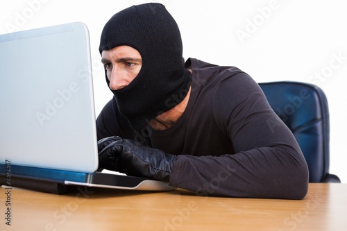 Burglar with balaclava hacking a laptop