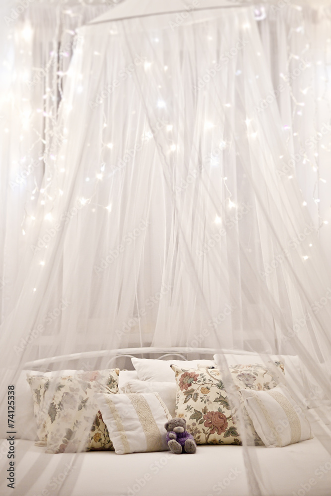 White cozy bed with vintage pillow and christmas lights